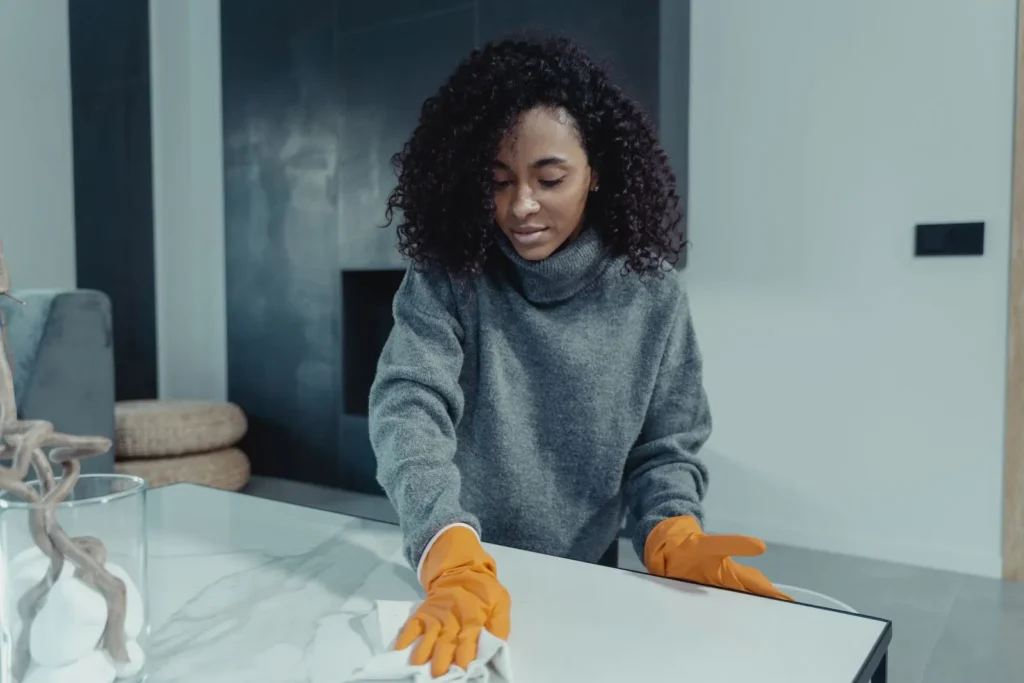 Personne portant des gants qui essuie une table dans un salon moderne et lumineux